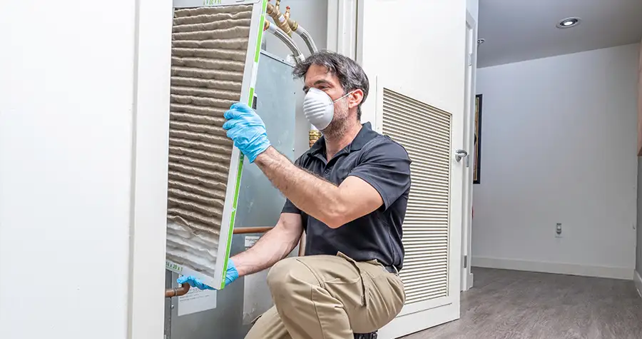 A man with a dust mask removing a grate from an air conditioner